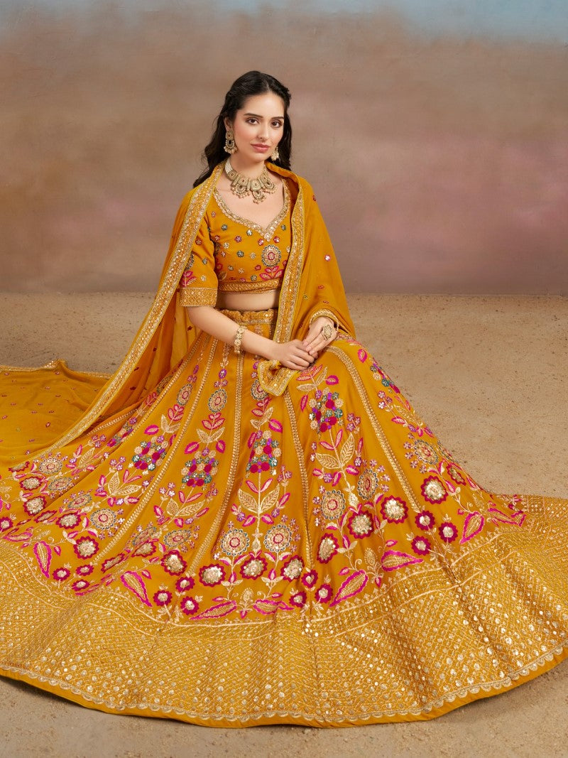 Full Front view of the model in sitting position showcasing mustard yellow floral zari embroidered flared lehenga choli with matching georgette dupatta