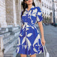 Woman wearing a blue and white floral dress on a city street.