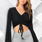 A woman wearing an ebony black, V-neck, bell sleeve, ruched front crop top with drawstrings and a slim fit.