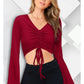 A woman wearing a maroon bell sleeves solid ruched front crop top with a V-neck and red earrings.