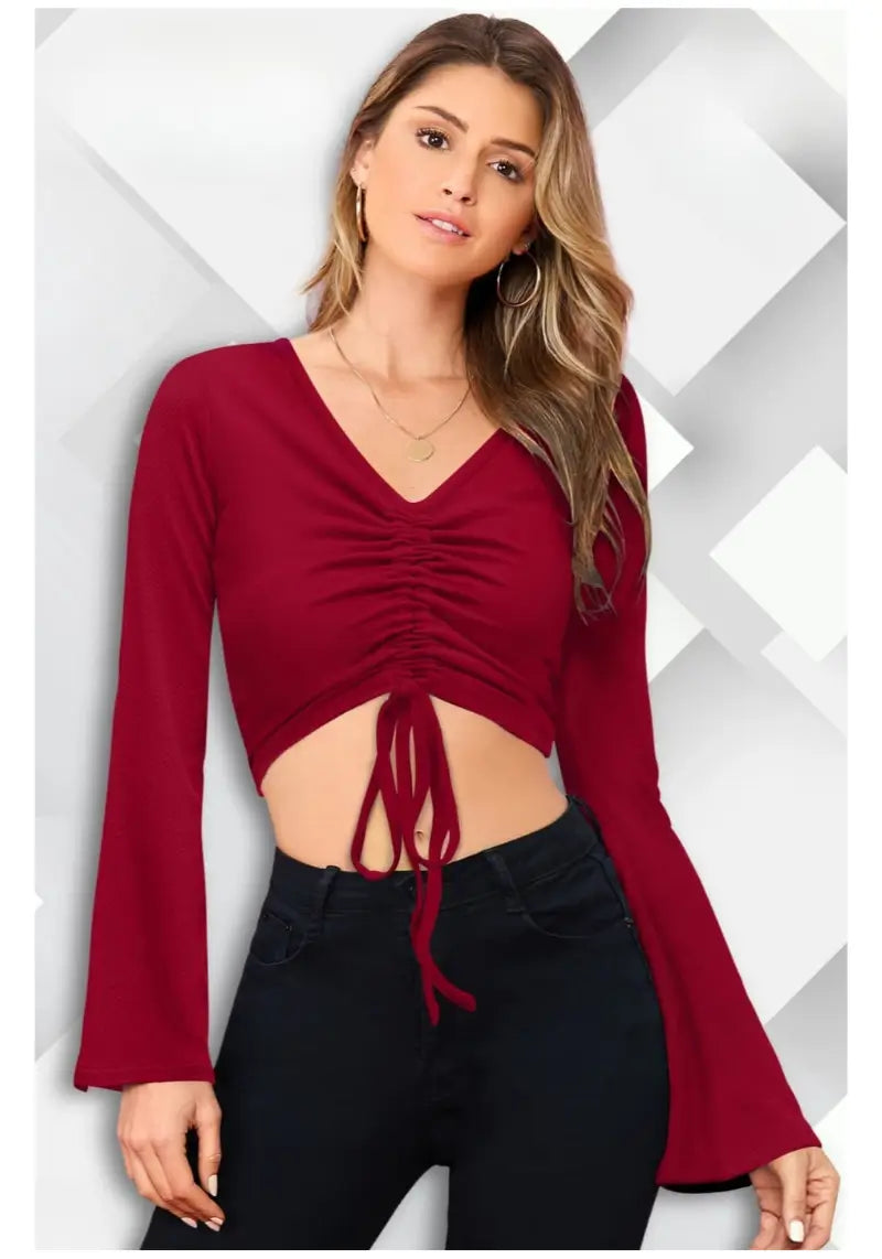 A woman wearing a maroon bell sleeves solid ruched front crop top with a V-neck and red earrings.