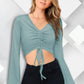 A woman wearing a pista green bell sleeves solid ruched front crop top with V-neck and a drawstring at the front.