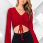 A woman wearing a red bell sleeves ruched drawstring front crop top with V-neck and a slim fit.